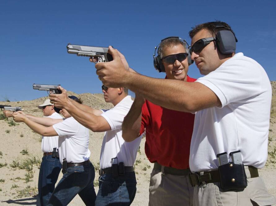 Outdoor firearm training: four participants focus on targets under instructor guidance at shooting range.