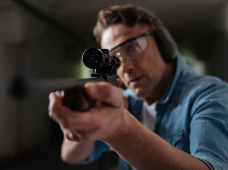 Concentrated shooter in denim jacket focuses on precision at an indoor shooting range.